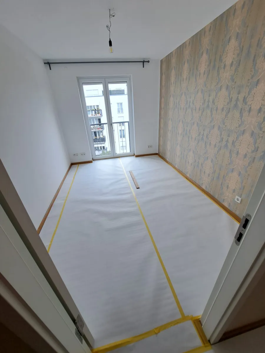 Zimmer mit gold-beiger Mustertapete vor der Renovierung, Boden bereits mit Vlies abgedeckt