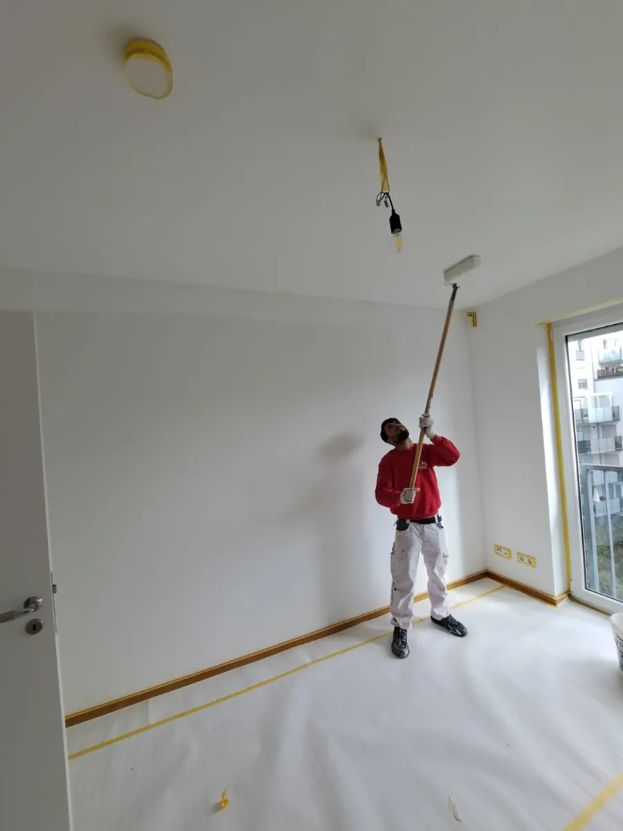 Maler von Andymen streicht eine Zimmerdecke mit der Teleskoprolle