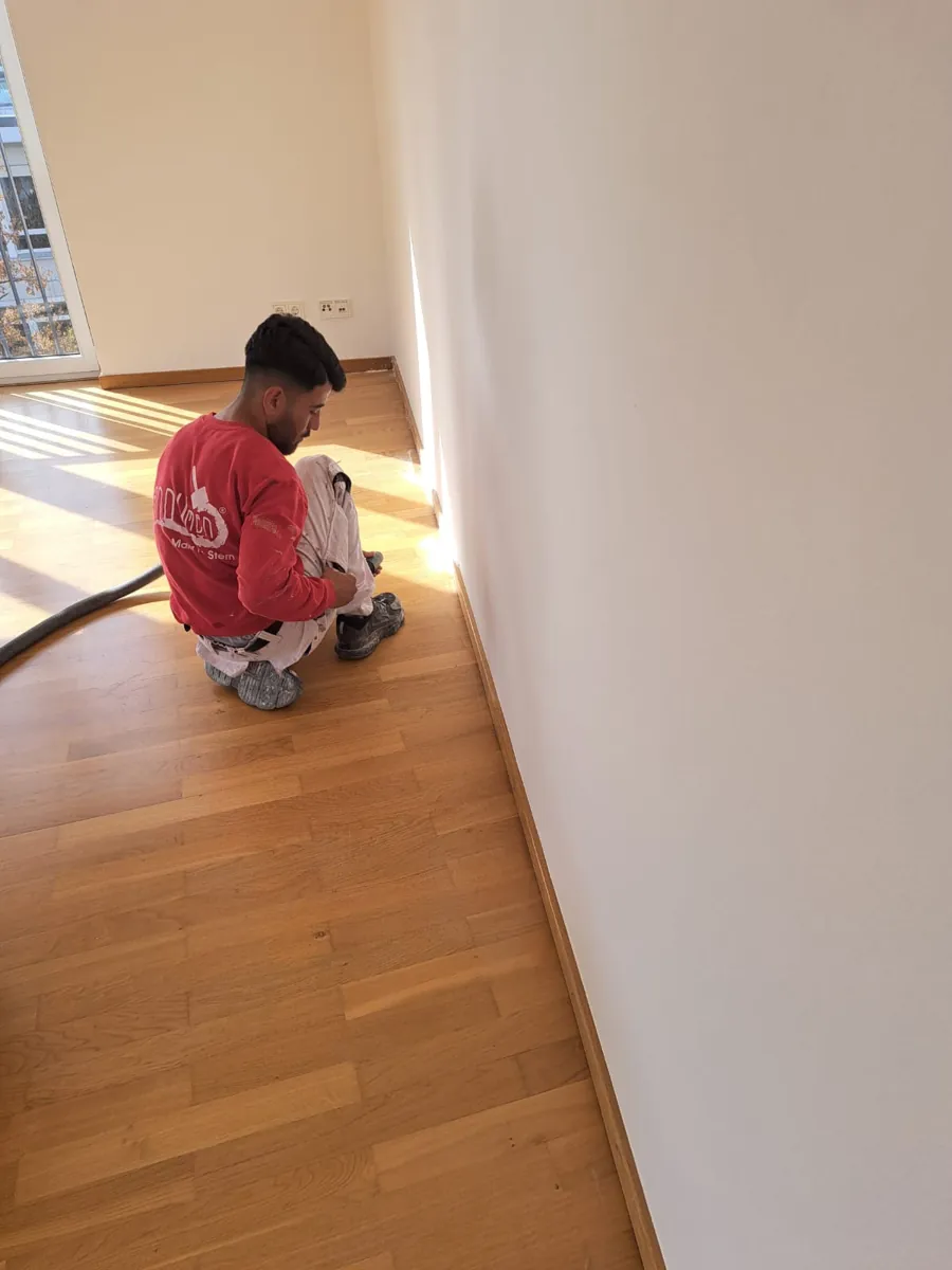 Handwerker arbeitet am Parkettboden entlang der Sockelleiste