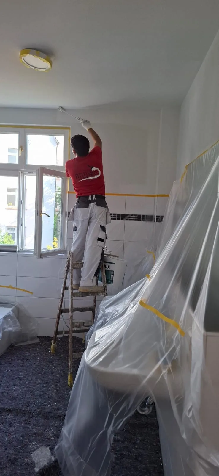 Andymen-Maler streicht Badezimmerdecke auf der Leiter, Badewanne foliert, in Marburg