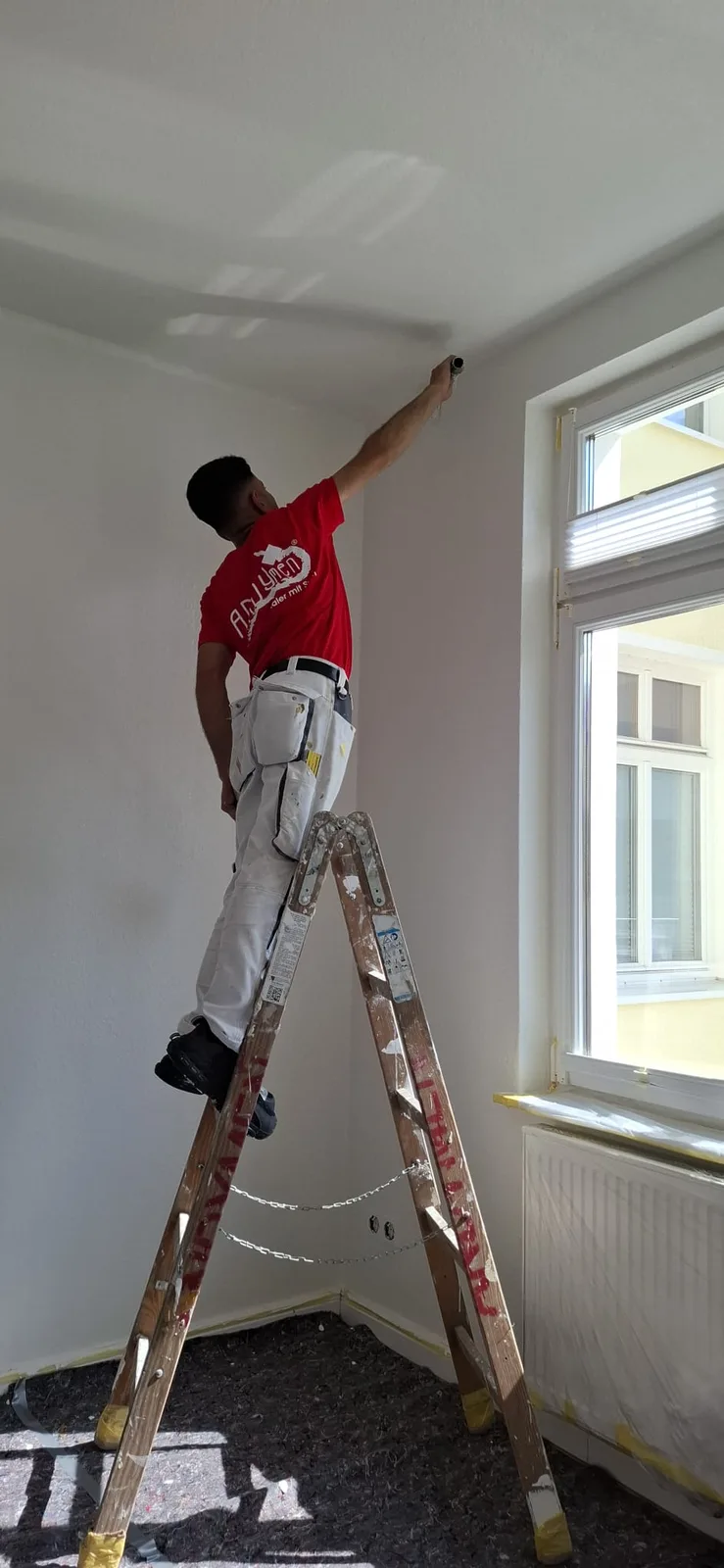 Andymen-Maler streicht Wand-Decken-Ecke am Fenster in Marburger Wohnung