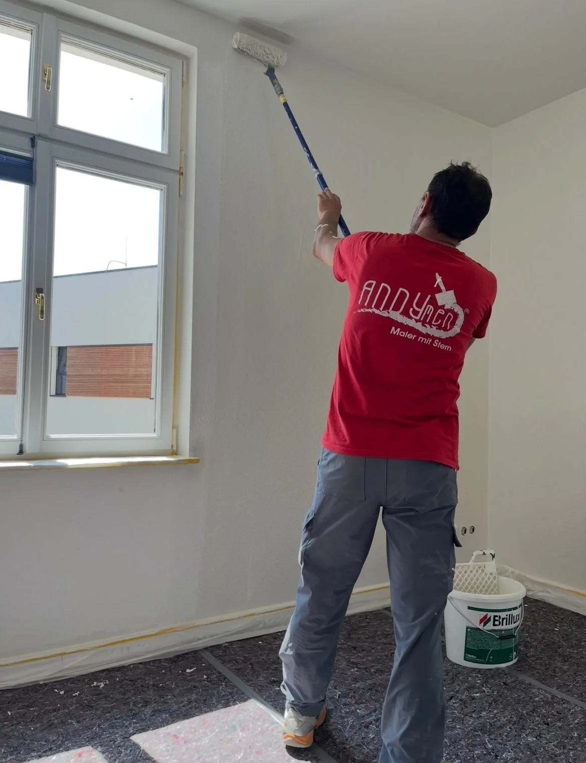 Maler streicht Wand mit Brillux und Verlaengerungsstange in Marburger Wohnung
