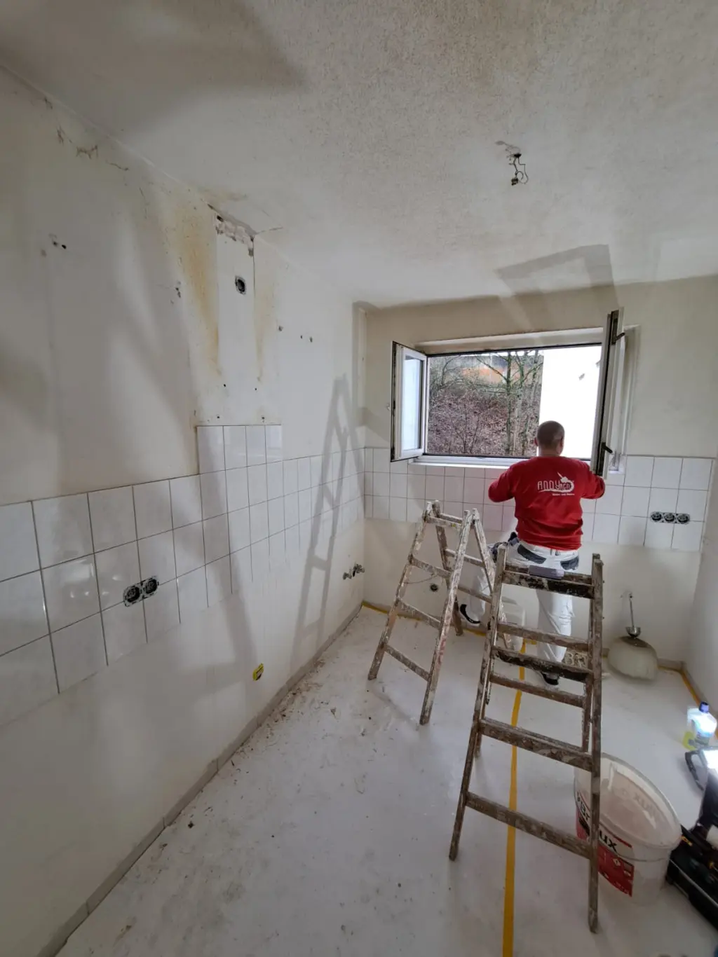 Kueche vorher — Maler streicht Decke und Waende ueber Fliesenspiegel
